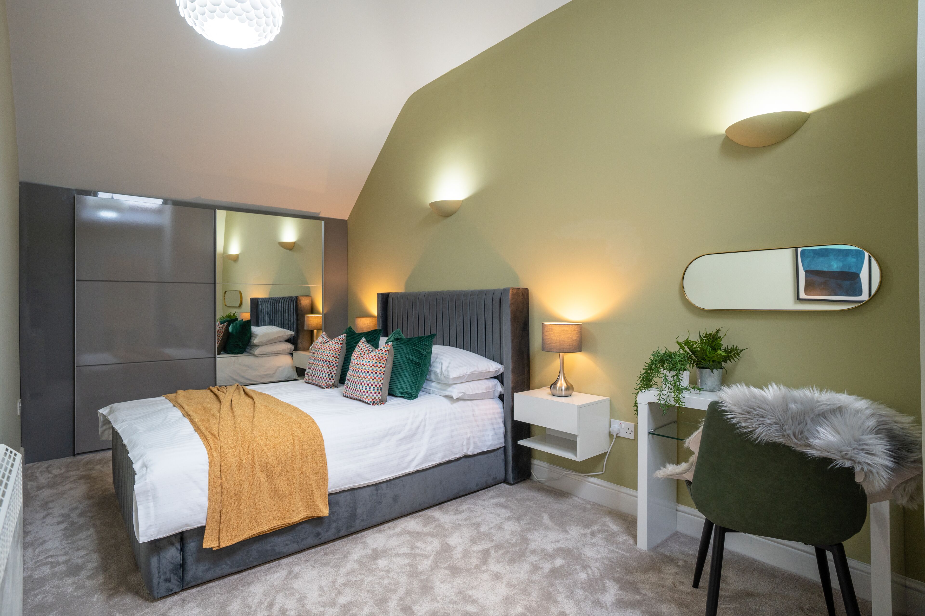 A modern bedroom with a bed, bedside tables, a chair, and a mirror.