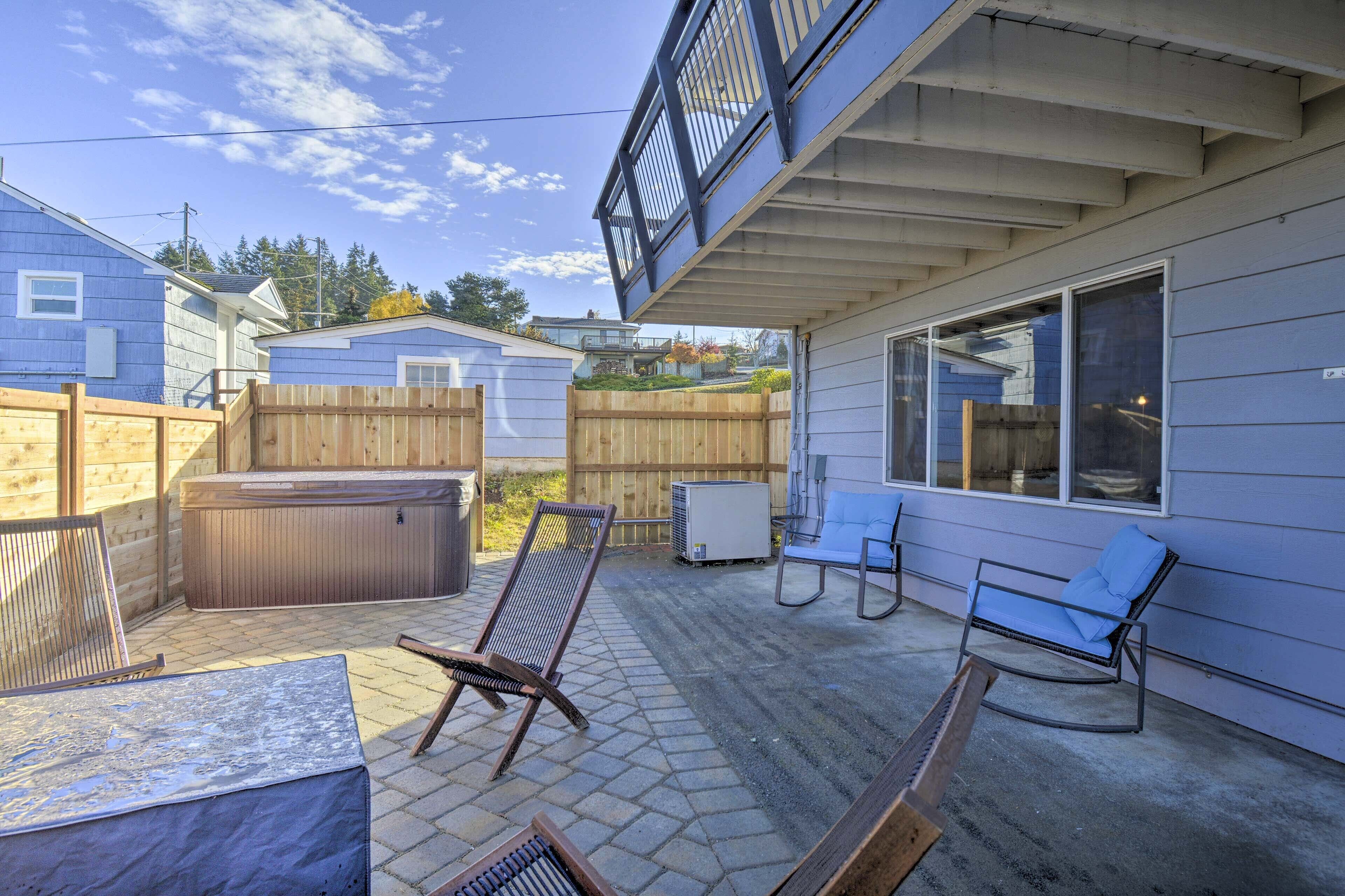 Un patio con mobiliario exterior, una bañera de hidromasaje y una zona cubierta con vistas a casas vecinas.