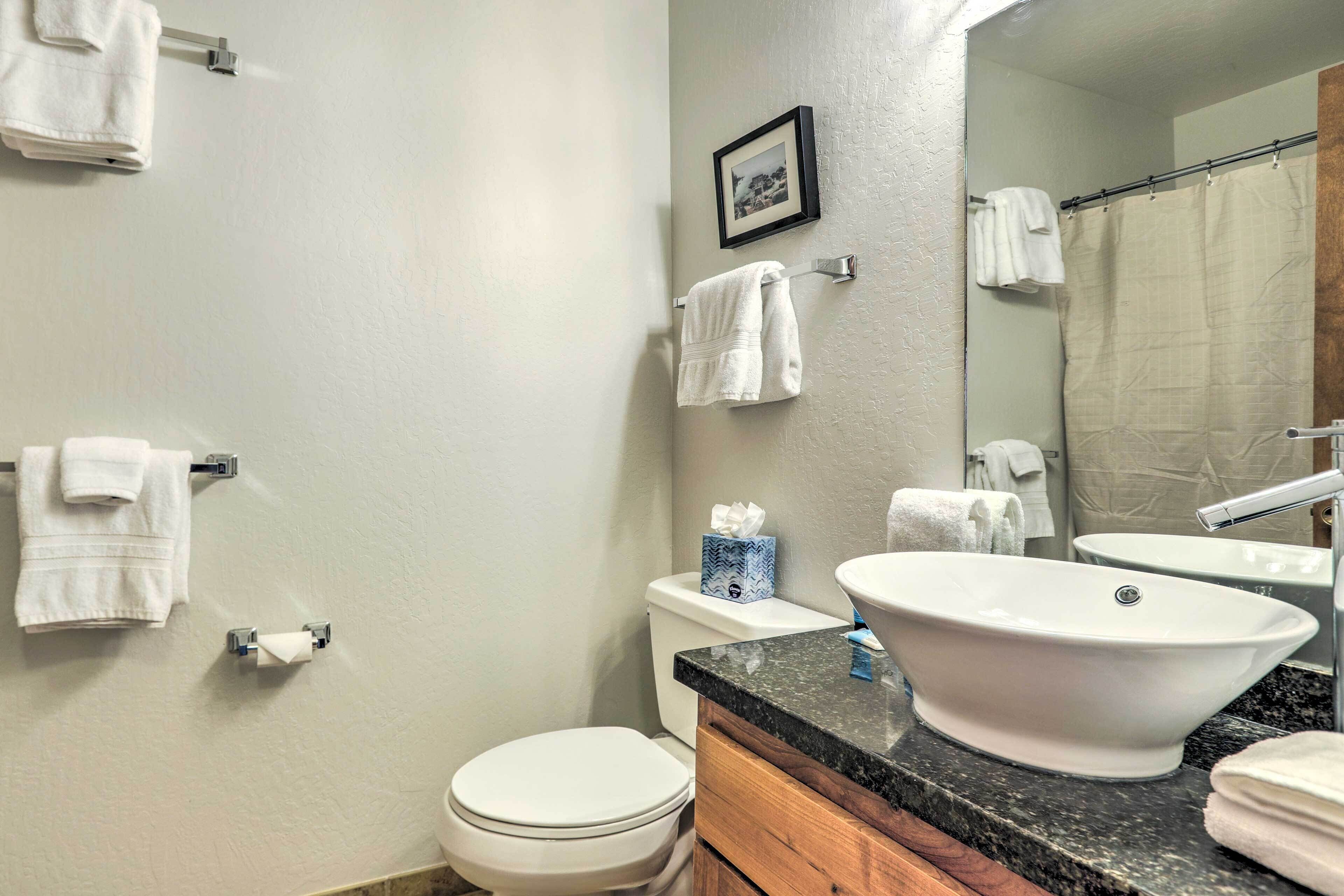 A bathroom with a toilet, sink, and mirror. There are towels hanging on the wall and a picture frame above the mirror.
