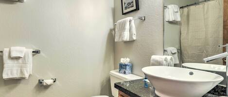 A bathroom with a toilet, sink, and mirror. There are towels hanging on the wall and a picture frame above the mirror.