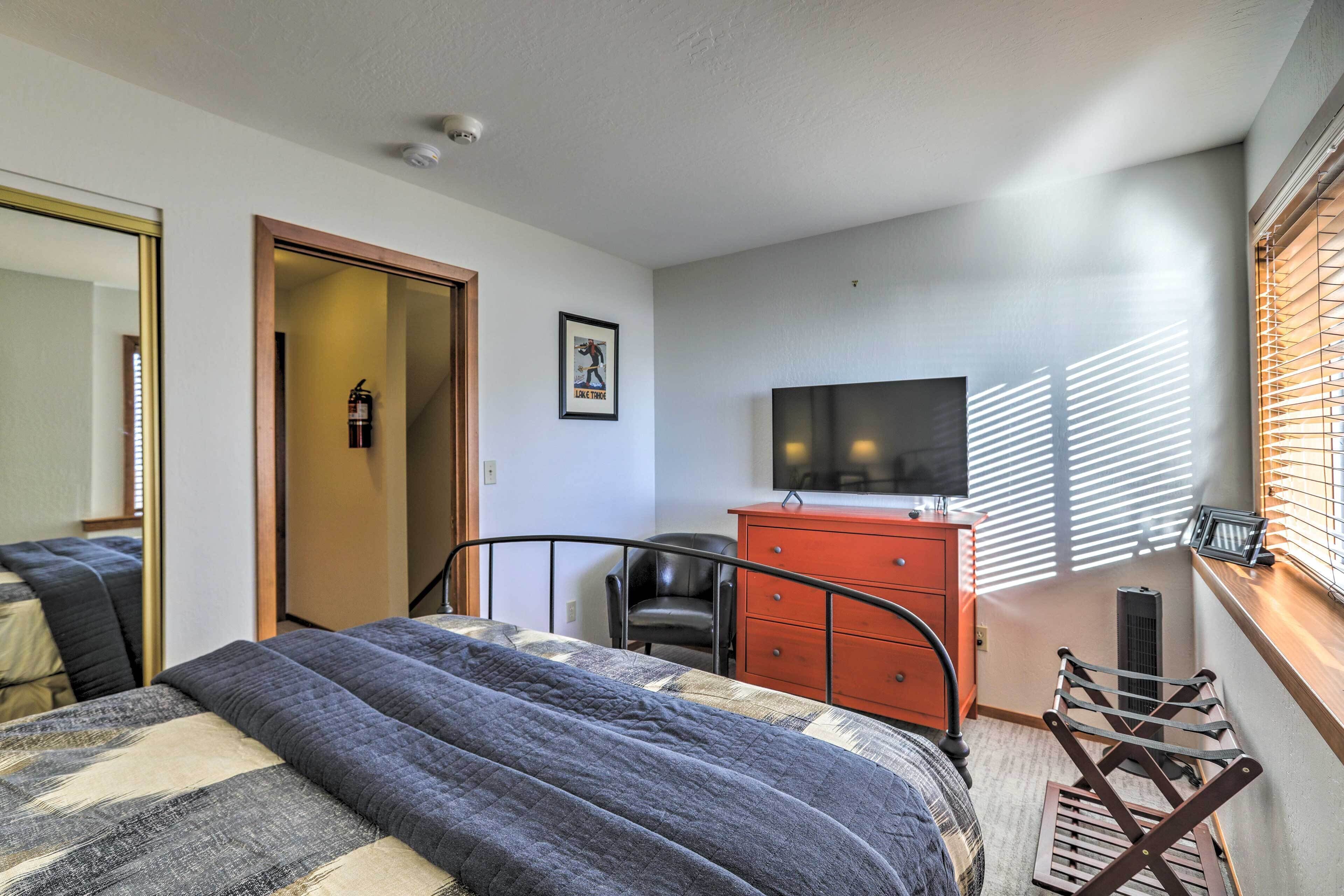 Une chambre à coucher comprenant un lit, une commode, une chaise, un téléviseur et une fenêtre avec des stores.