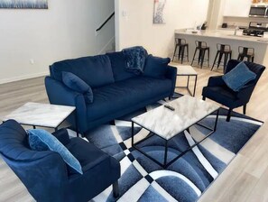 Relax in this stylish living room with a sofa, armchair, and coffee table, plus a kitchen area with a bar stool.