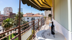 A balcony with a table displaying a bottle of wine and a glass, overlooking a cityscape with buildings and palm trees. - Casa Laura Follonica  200 metres from the sea/beach Wifi air/condition tv/sat (Follonica)