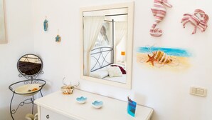 A room with a bed, a bedside table with decorative items, a mirror, and wall decorations including a seahorse and a beach scene. - Casa Laura Follonica  200 metres from the sea/beach Wifi air/condition tv/sat (Follonica)