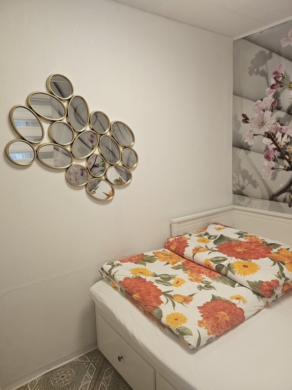 A bedroom with a bed, a wall-mounted mirror arrangement, and a floral-patterned bedspread.