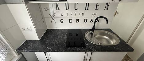 A modern kitchen with a black countertop, stainless steel sink, and a backsplash with German text.