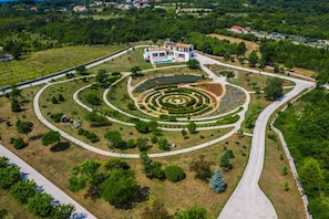 Vista aérea de una casa moderna con un jardín circular, rodeada por un camino pavimentado y una carretera.