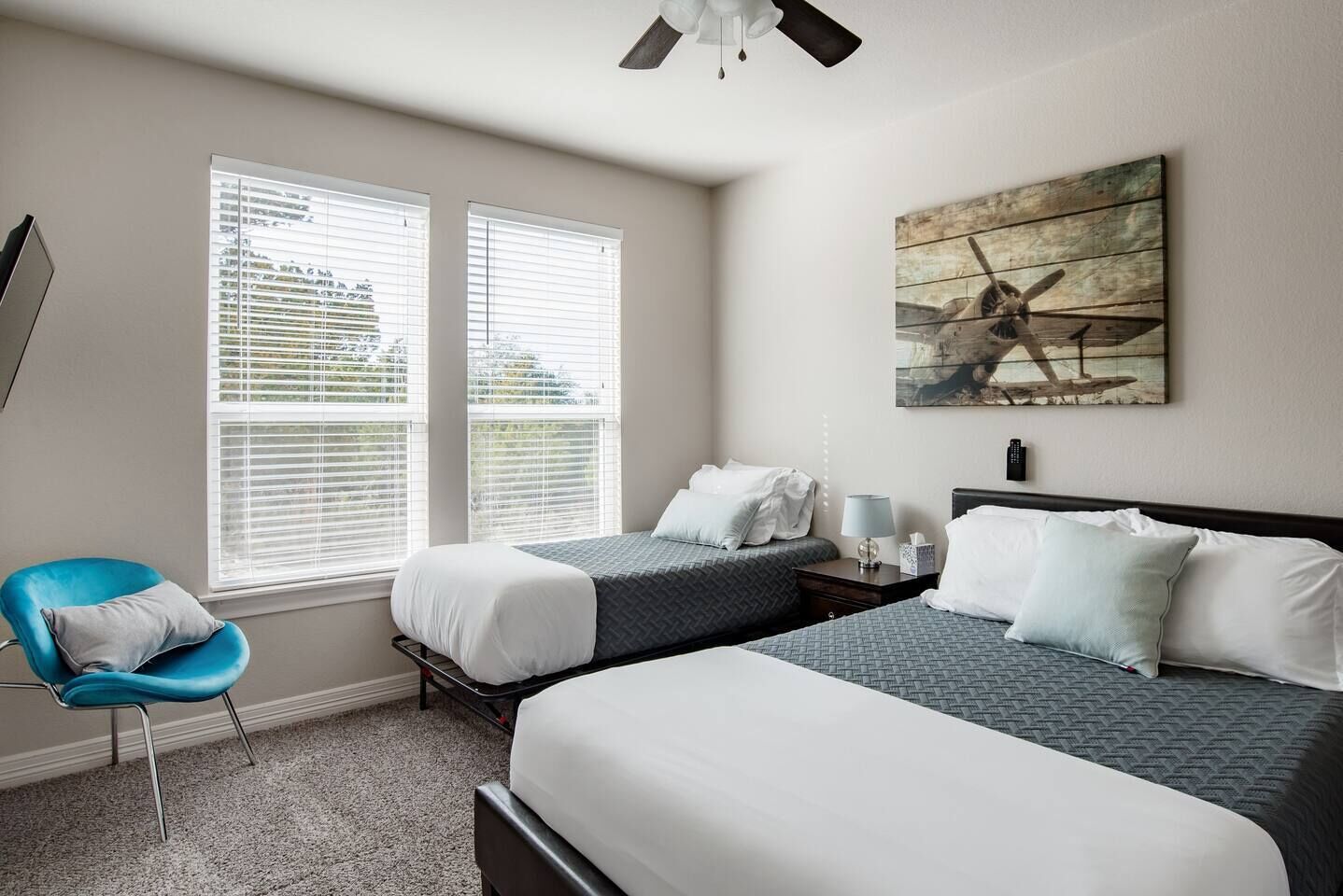 A hotel room with two beds, a blue chair, and a painting on the wall.