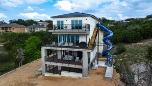 Een meerlaags huis met een balkon, een glijbaan en uitzicht op omliggende huizen.