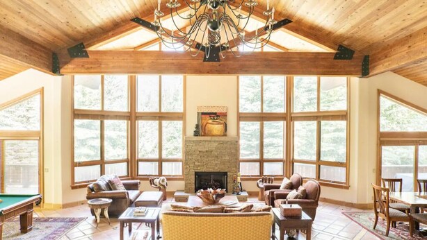 A spacious living room with a fireplace, large windows, and a high ceiling with exposed beams. - Stunning mountainside home in West Vail (Vail)
