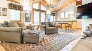 A spacious living room with a high wooden ceiling, large windows, and a dining area with a kitchen in the background. - Stunning mountainside home in West Vail (Vail)