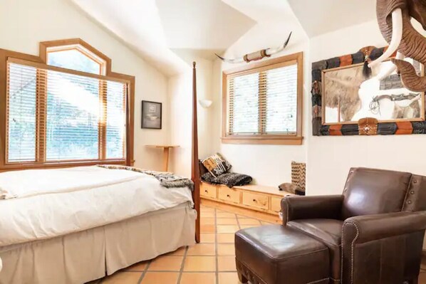 A bedroom with a bed, a wooden bench, a leather armchair, and a large window with blinds. - Stunning mountainside home in West Vail (Vail)