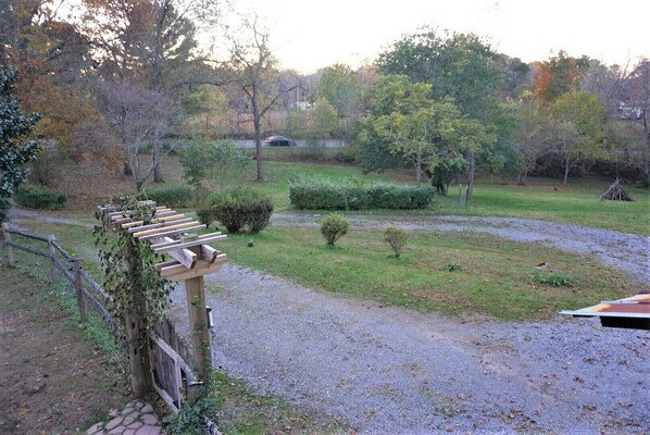 Un chemin de gravier bordé d’une pergola en bois recouverte de lierre, le tout entouré de pelouse et d’arbustes bien entretenus.