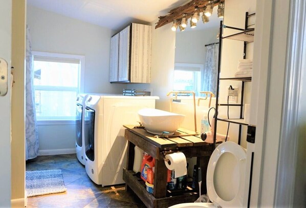 A compact bathroom with a washing machine, a sink with a large bowl, and a toilet.