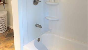 Un baño moderno con bañera, zona de ducha y inodoro. Hay repisas con artículos de aseo.