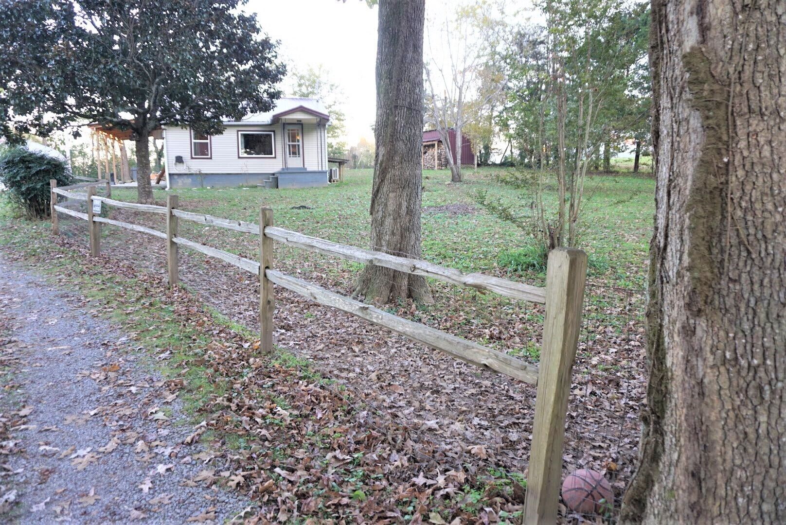 A wooden fence in a wooded area with a house in the background.