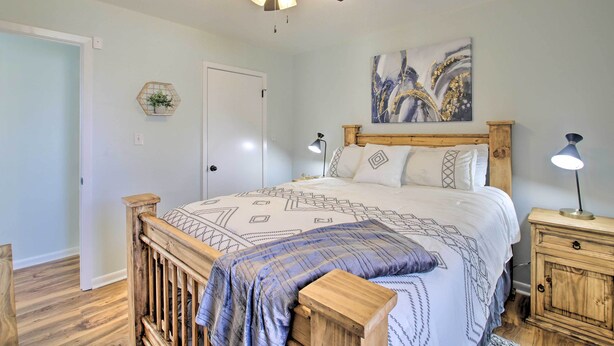 A bedroom with a wooden bed frame, a ceiling fan, a bedside table with a lamp, and a wall-mounted artwork.