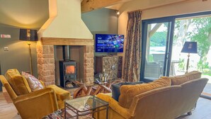 A cozy living room with a stone fireplace, comfortable seating, a flat-screen TV, and a view of the outdoors. - Waters Edge, a romantic cottage with stunning views of Talkin Tarn (Brampton)