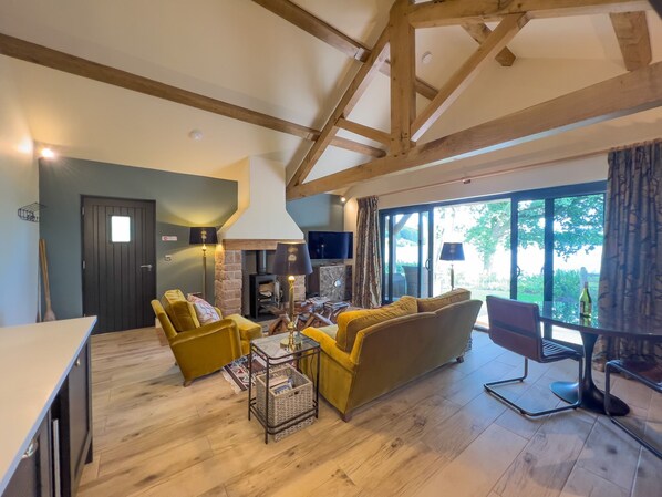 A cozy living room with a fireplace, yellow armchairs, a sofa, and a dining area. - Waters Edge, a romantic cottage with stunning views of Talkin Tarn (Brampton)