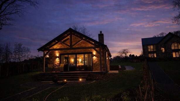 A stone cabin with a porch, large windows, and a chimney. - Waters Edge, a romantic cottage with stunning views of Talkin Tarn (Brampton)