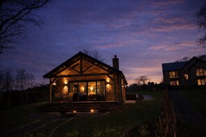 A stone cabin with a porch, large windows, and a chimney. - Waters Edge, a romantic cottage with stunning views of Talkin Tarn (Brampton)