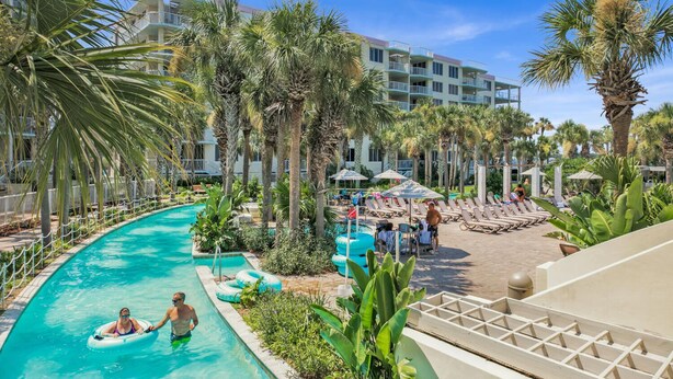 A pool area with lounge chairs, palm trees, and a hotel building in the background. - Remodeled Beachfront 🐠🦀 Destin West's Best 😎😎 Beach Service Inc ⛱️⛱️NEW EVERYTHING (Fort Walton Beach)