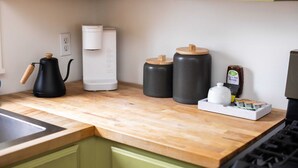 Eine Küche mit einer Holzausziehtischplatte, einer Kaffeemaschine, zwei Behältern mit Deckeln, einem Honigglas und einem Tee-Service.