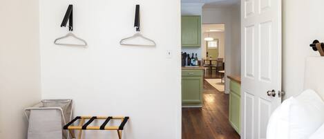 A bedroom with a bed, a drying rack, and a view into the kitchen area.
