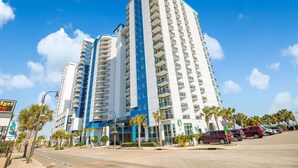 A tall hotel with multiple floors, a prominent blue and white color scheme, and a parking lot with several cars. - Oceanfront penthouse, centrally located, 4 bed/ 4 bath (Myrtle Beach)