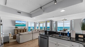 A modern kitchen with a dishwasher, a dining area with a table and chairs, and a large window with a view of the ocean. - Oceanfront penthouse, centrally located, 4 bed/ 4 bath (Myrtle Beach)