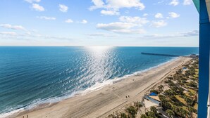 A beach with a pier extending into the ocean, a clear sky, and a few people walking along the shore. - Oceanfront penthouse, centrally located, 4 bed/ 4 bath (Myrtle Beach)