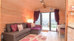 A cozy cabin interior with a wooden ceiling, a sofa with cushions, a dining area, and a view of the outdoors. - Lovies Place - Crossgate Luxury Glamping (Penrith)