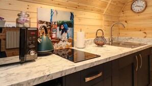 A kitchen with wooden walls, a marble countertop, a kettle, a sink, a clock, and a painting of a man shearing sheep.