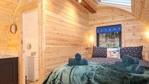 A cozy wooden cabin bedroom with a bed, towels, a window, and a bathroom.