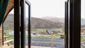 A wooden deck with a view of a rural landscape, including a house and hills.
