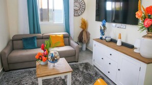 A living room with a sofa, a coffee table with a vase of flowers, a TV, and a clock on the wall.