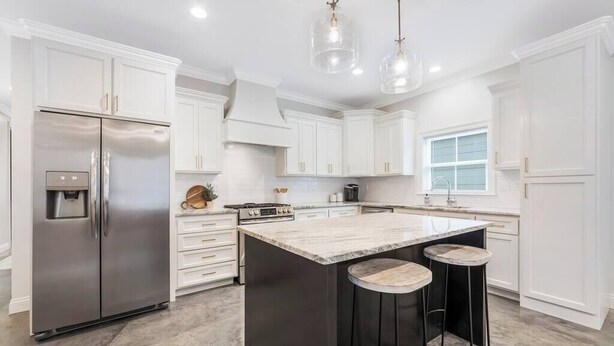 A modern kitchen with white cabinets, a stainless steel refrigerator, a central island with stools, and pendant lighting. - Charming Cottage -3BR - A+ Location - est.2019 (Lafayette)