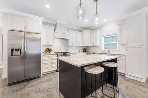 A modern kitchen with white cabinets, a stainless steel refrigerator, a central island with stools, and pendant lighting. - Charming Cottage -3BR - A+ Location - est.2019 (Lafayette)