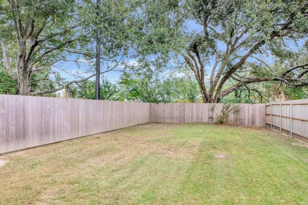 A fenced backyard with a grassy area and trees.