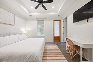 Un dormitorio con cama, escritorio, silla, ventilador de techo y puerta.