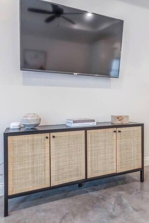 A flat-screen TV mounted on a wall, a black console with wicker panels, and a ceiling fan. - Charming Cottage -3BR - A+ Location - est.2019 (Lafayette)