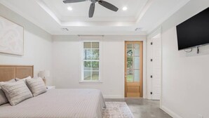 A bedroom with a bed, a ceiling fan, a TV, a window, and a door. - Charming Cottage -3BR - A+ Location - est.2019 (Lafayette)