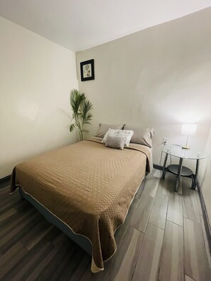 Relax in a cozy retreat with a large bed, compact workspace, and a touch of greenery.