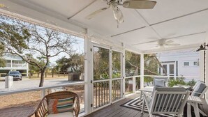 A covered porch with wooden flooring, white railings, and a ceiling fan. There are outdoor seating areas with chairs and a table. - The Salty Pig- Dog Friendly- 4 Bikes Included (Santa Rosa Beach)