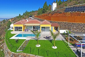 Una casa moderna con piscina, patio y paneles solares en el techo.