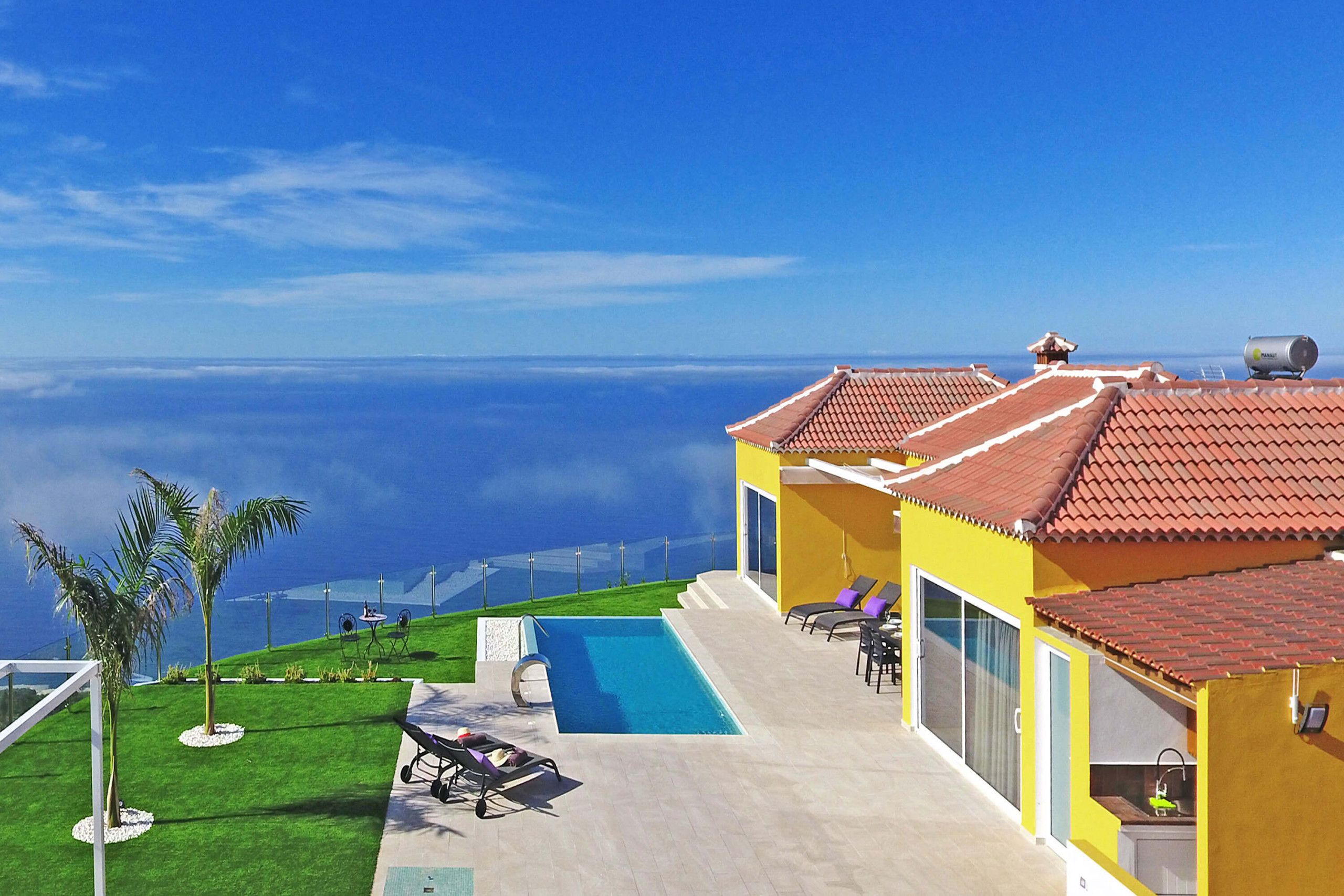 Une maison moderne dotée d’une piscine, d’un patio avec des chaises longues et d’une vue sur l’océan.
