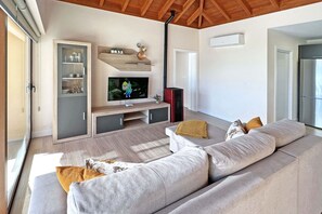 Una sala de estar moderna con un sofá grande de color gris, un televisor de pantalla plana y un techo de madera.
