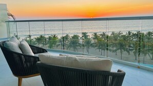 A balcony with a view of the sunset over the ocean, featuring a wicker chair and a cushion. - Beachfront 3BR-3BA SunsetParadise (Flamingos)