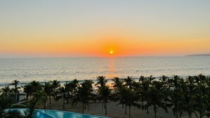 A beach with palm trees and a pool, overlooking the ocean at sunset. - Beachfront 3BR-3BA SunsetParadise (Flamingos)