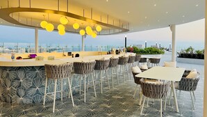 A modern bar area with a curved counter, multiple bar stools, and a view of the cityscape. - Beachfront 3BR-3BA SunsetParadise (Flamingos)